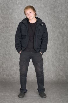 The young guy in a jacket standing on a grey background