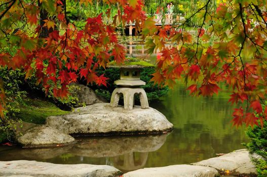 Beautiful Japanese Garden with red maple overhanging Zen lake and stone lantern post structure