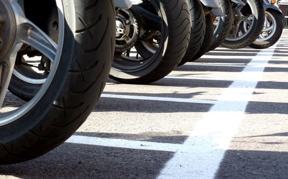 Wheels of many motorbikes in a parking with white line on the ground