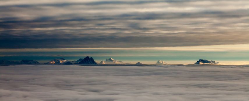Distant snowcapped mountain peaks between two layers of clouds.