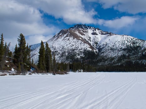 Ski-doo track on windblown snowy surface of frozen mountain lake in winter wonderland of Yukon Territory, Canada