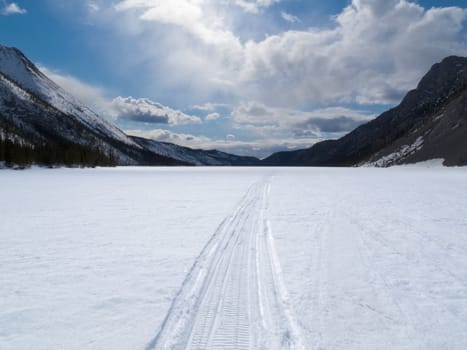Ski-doo track on windblown snowy surface of frozen mountain lake in winter wonderland of Yukon Territory, Canada