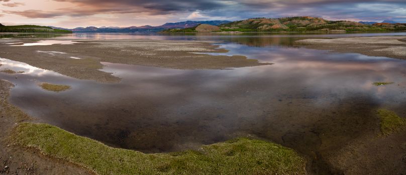 Dramatic Cloudscape gets reflected on calm surface of shallow shore of Lake Laberge, Yukon Territory, Canada