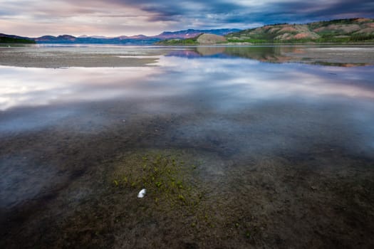 Dramatic Cloudscape gets reflected on calm surface of shallow shore of Lake Laberge, Yukon Territory, Canada
