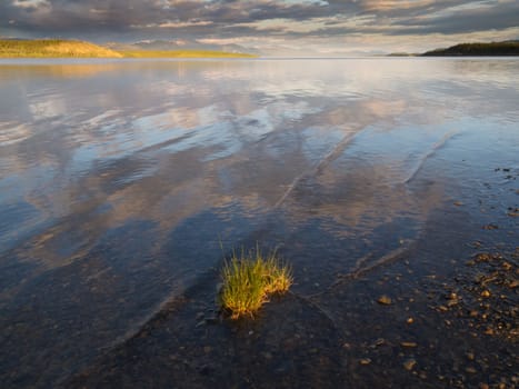 Dramatic Cloudscape gets reflected on calm surface of shallow shore of Lake Laberge, Yukon Territory, Canada