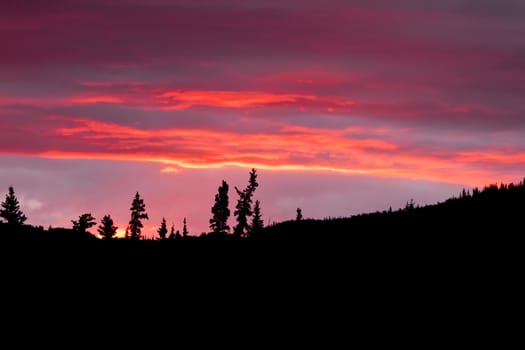 Cloudy sunset sky on fire over silhouette of forested hills.