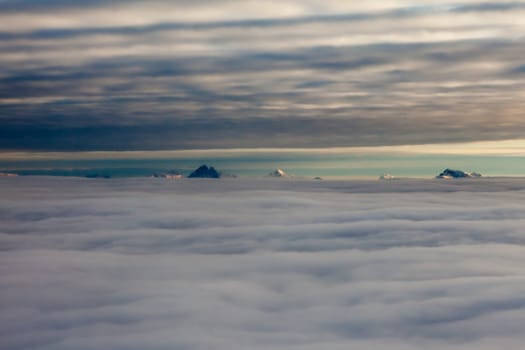 Distant snowcapped mountain peaks between two layers of clouds.