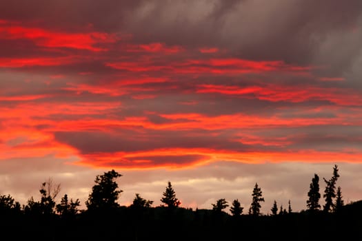 Cloudy sunset sky on fire over silhouette of forested hills.