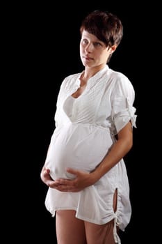 Pregnant young woman in a white shirt on the black background
