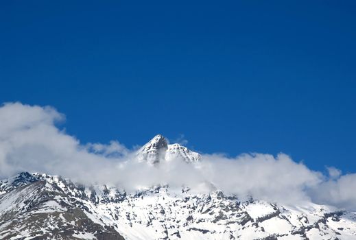 snowed peak of a mountain surrounded by small cloud, a lot of blue for copy-space