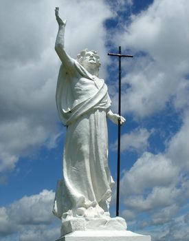 White sculpture of jesus holding y cross and with right and up with cloudy sky behind