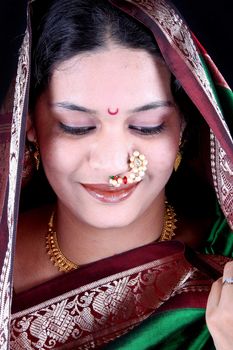 A portrait of a shy Indian woman wearing a green sari, on a black background.