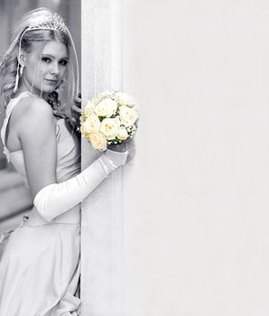 Attractive blond young adult bride leaning on wall with copy space.