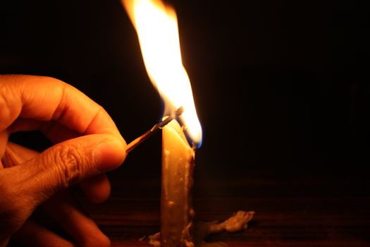 A background with a view of a human hand lighting a candle with a matchstick, on black background.