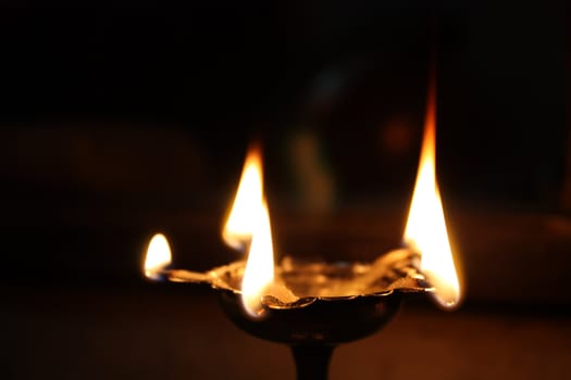 A traditional holy oil-lamp lit in a Hindu temple. The lamp is made of a long metal stem & floral bowl, with five places for wick / flames.