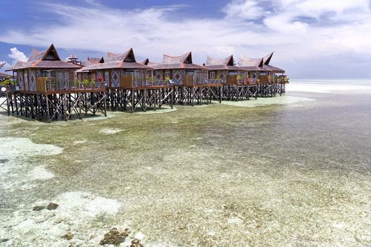 Image of huts on stilts on a remote Malaysian tropical island with deep blue skies and crystal clear waters.