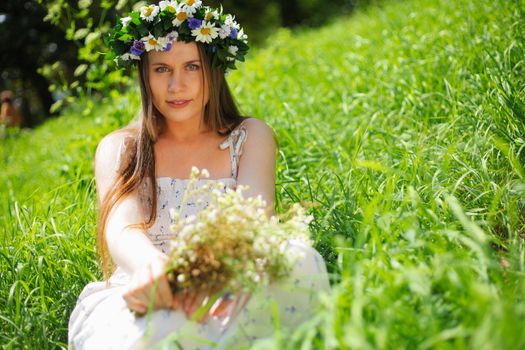 Portrait of a girl with circlet of flowers. She is sitting in a green meadow