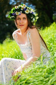 Portrait of a girl with circlet of flowers. She is sitting in a green meadow