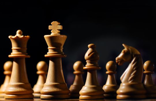 Image shows chess pieces around the white King, photographed from a low angle and with selective focusing on the king.