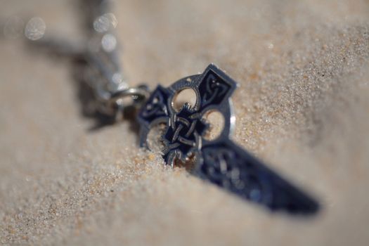A silver and blue celtic cross on the sandy dunes.