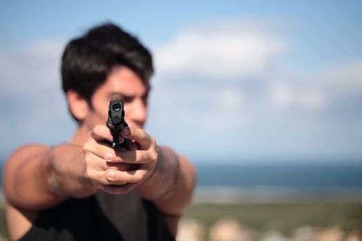 A young, robust man, in his 20's with dark hair pointing 2 pistols to the camera.