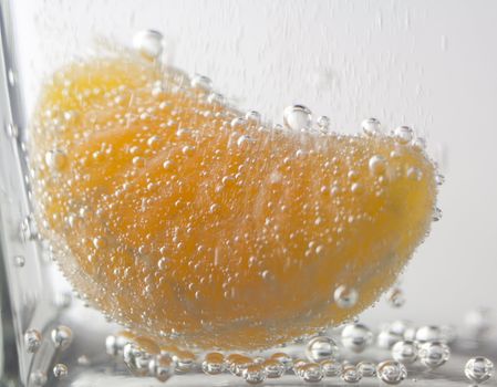 close-up slice of tangerine in water with bubbles