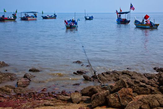 A view of Malaysian fishing boats with rock formations in the foreground