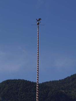 Antique weather cock in front of blue sky and forest