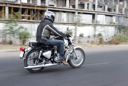 Motor biker breaks road rules by undertaking on the inside lane, horizontal landscape, copy space and crop space. Tarmac roads with white markings, derelict factory on roadside undergrowth