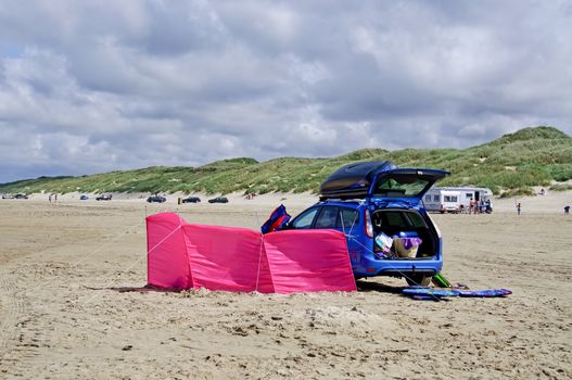 A blue family car on the beach with a pink windscreen