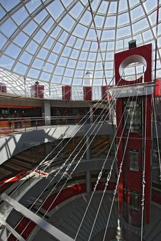 Huge hall of modern shopping centre with the glass lift, hours on a floor and a transparent glass dome