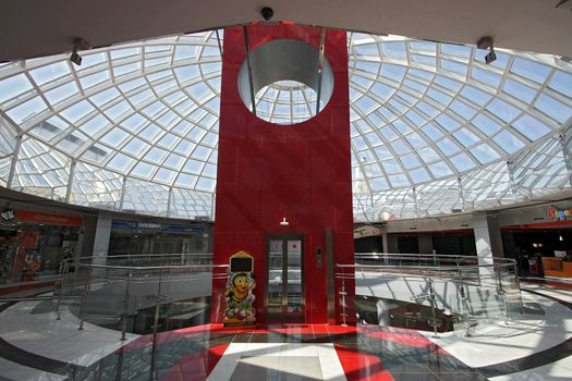 Huge hall of modern shopping centre with the glass lift and a transparent glass dome