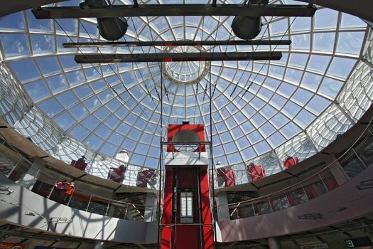 Huge hall of modern shopping centre with the glass lift and a transparent glass dome
