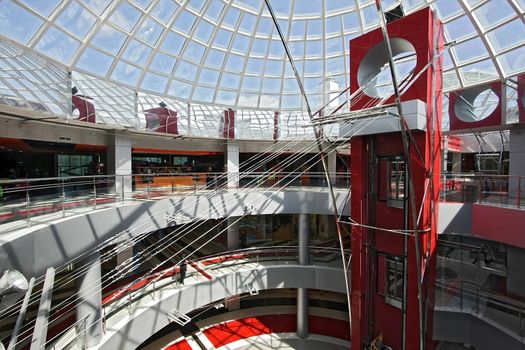 Huge hall of modern shopping centre with the glass lift and a transparent glass dome