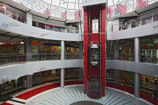 Huge hall of modern shopping centre with the glass lift and a transparent glass dome