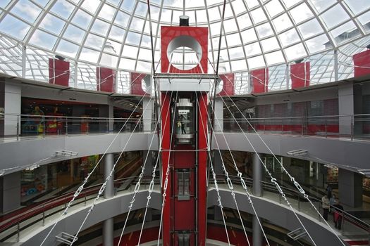 Huge hall of modern shopping centre with the glass lift and a transparent glass dome