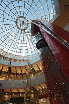 Huge hall of modern shopping centre with the glass lift and a transparent glass dome