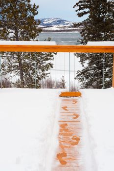 Footsteps of person trying to escape winter by jumping over railing of snow covered wooden deck.