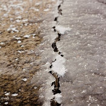 Cracked thick layer of ice with hoar-frost ice crystals forming on edge.