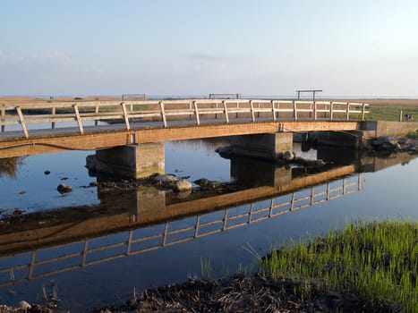 Simple wooden bridge path over a small river with reflection in the water