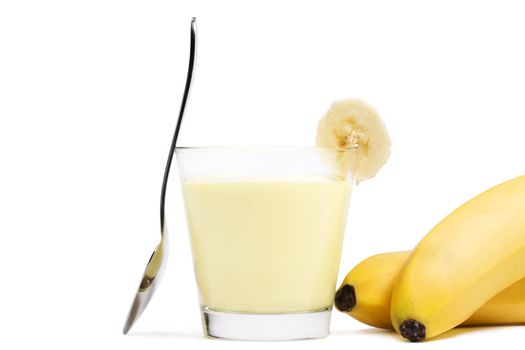 banana milkshake with a piece of banana a spoon and bananas aside on white background