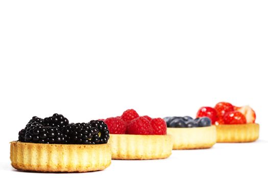 blackberries and other wild berries in tartlet cakes on white background