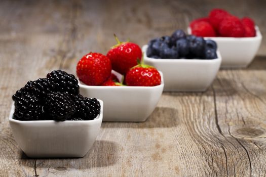 some bowls filled with wild berries on wooden background blackberries in front