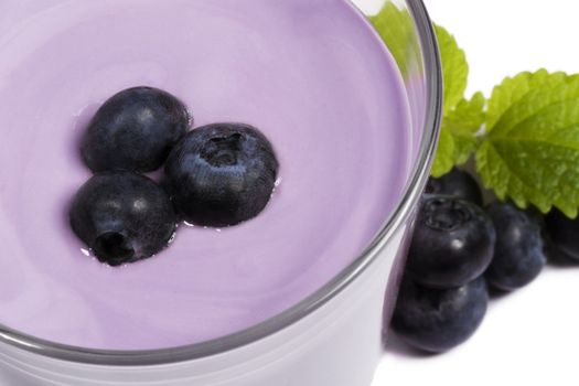 blueberries on top of a blueberry milkshake with blueberries and melissa aside on white background