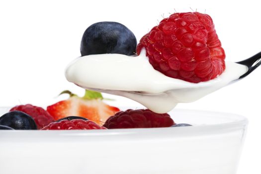 raspberry and blueberry on a spoon with yogurt in front of a dessert on white background