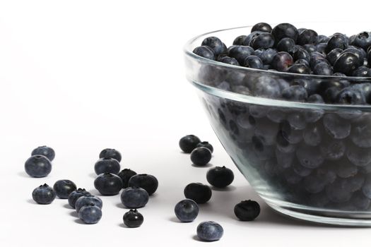 bowl full with a lot of blueberries with some blueberries aside on white background