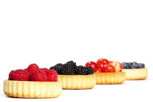 raspberries in tartlet cake in front of other tartlet cakes with wild berries on white background