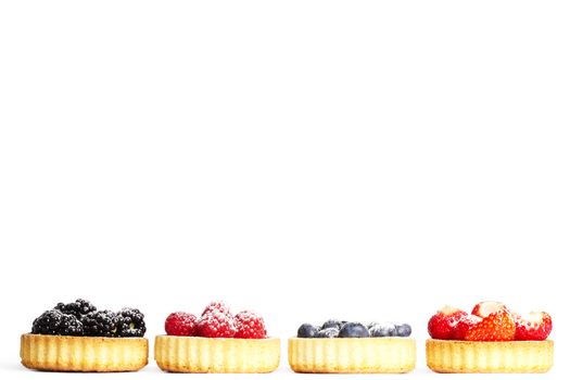 row of tartlets with sugar covered wild berries on white background