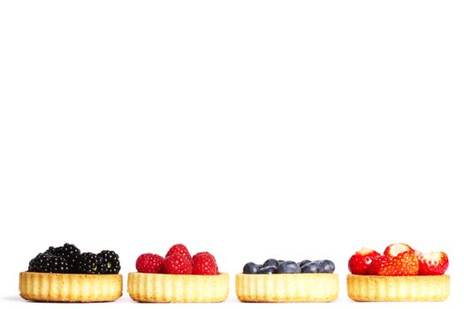 row of tartlets with wild berries on white background