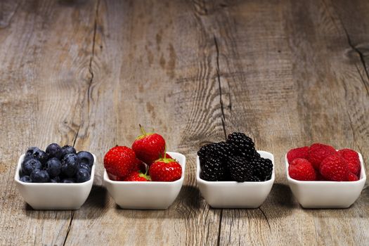row of wild berries in bowls on wooden background